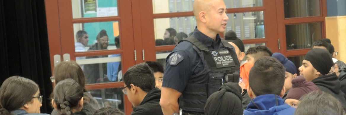 A male RCMP anti-gang officer stands in front of a group of young students.