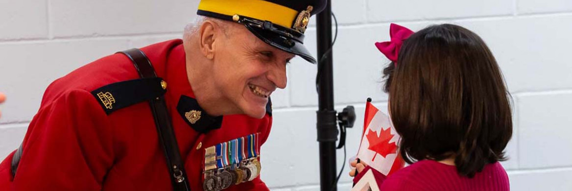Une fillette reçoit un drapeau canadien des mains d'un membre de la GRC en tunique rouge.