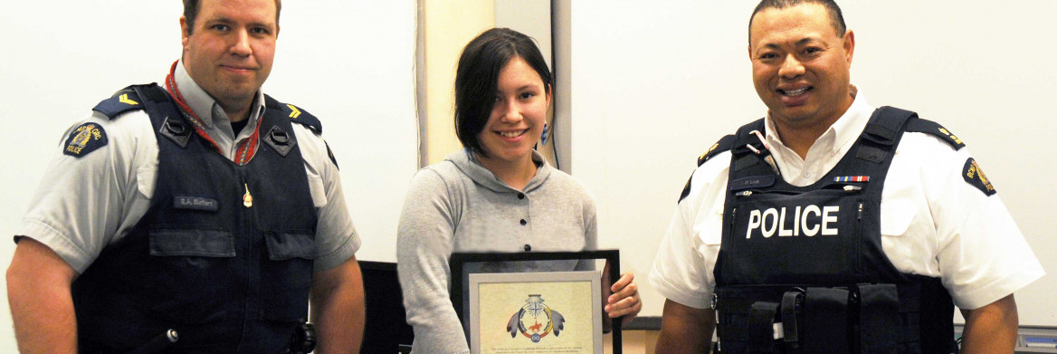 Deux policiers debout à côté d'une adolescente qui tient un cadre de l'emblème.