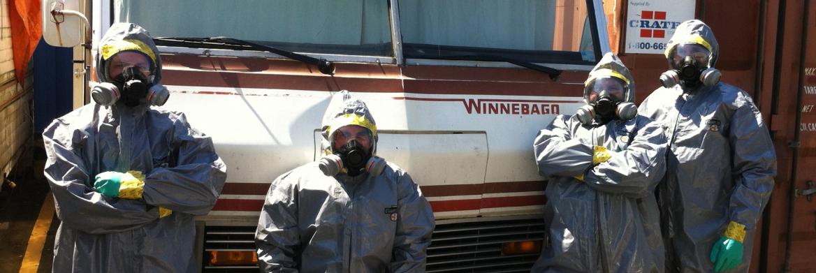 Four people wearing full hazmat gear stand outside of an RV.