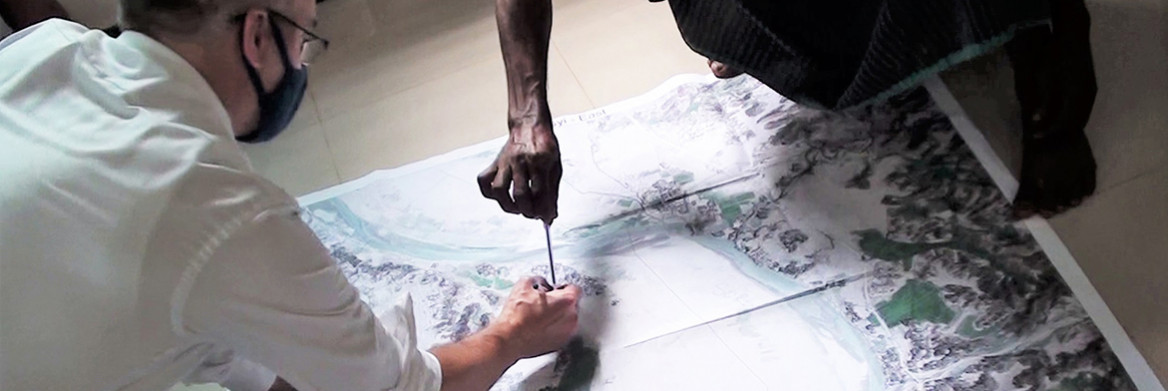 Un homme portant un masque et une femme examinent une grande carte topographique sur un plancher.