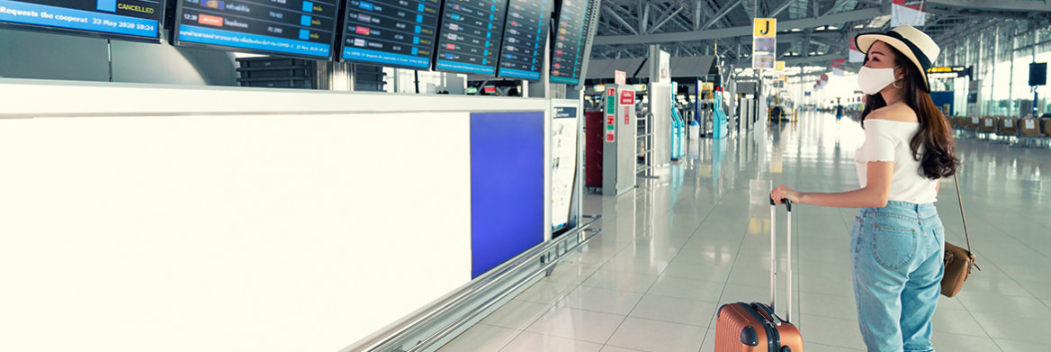 Une voyageuse tenant une valise regarde un panneau d'information sur les vols dans un aéroport.