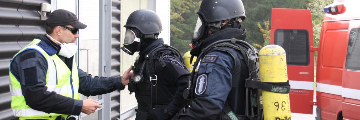Homme qui parle à deux policiers équipés de masques et de réservoirs d'oxygène. 
