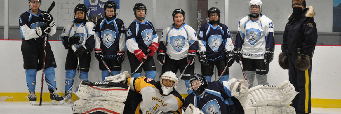 Des joueuses de hockey vêtues de chandails bleu et blanc se font photographier en compagnie d'un policier de la GRC sur une patinoire intérieure. 