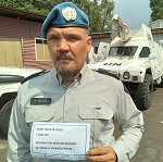 A Canadian police officer stands in front of a white UN truck, holding a sign that reads, 