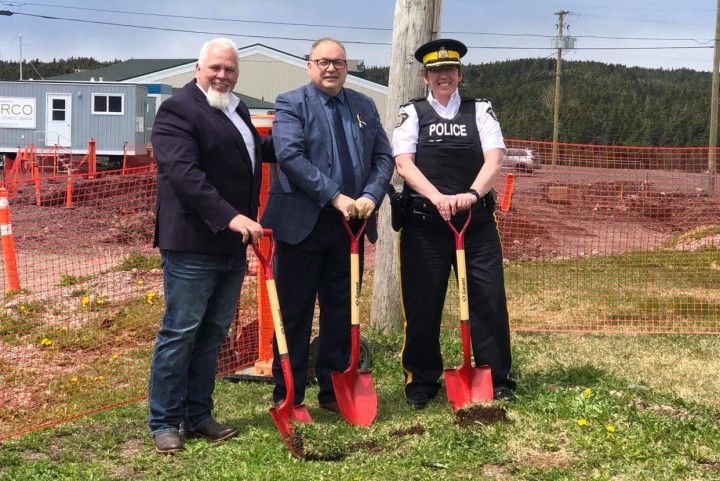 Three people, one in police uniform, dig shovels into the ground. 