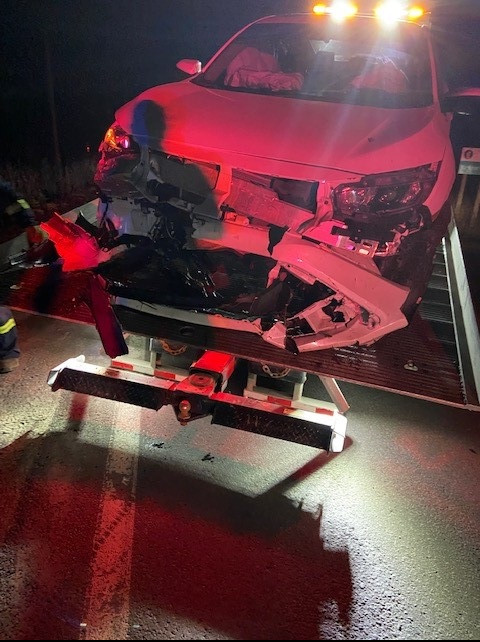 Une Honda Civic blanche ayant subi des dommages importants à l'avant et dont les coussins gonflables ont été déployés se trouve sur une remorqueuse, alors qu'il fait nuit.