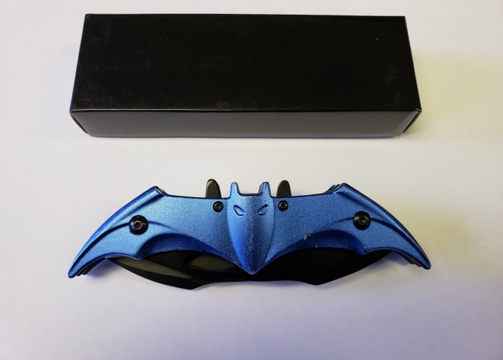 A black case sits above a blue and black prohibited knife in a closed position. The knife resembles a bat.