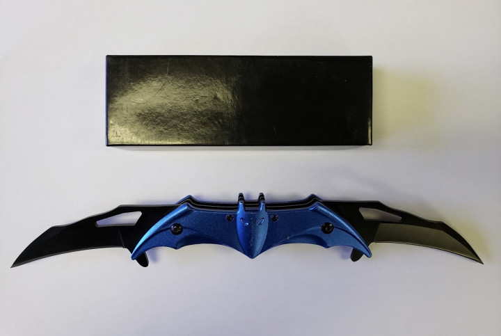A black case sits above a blue and black prohibited knife in an open position with two blades ejected. The knife resembles a bat.