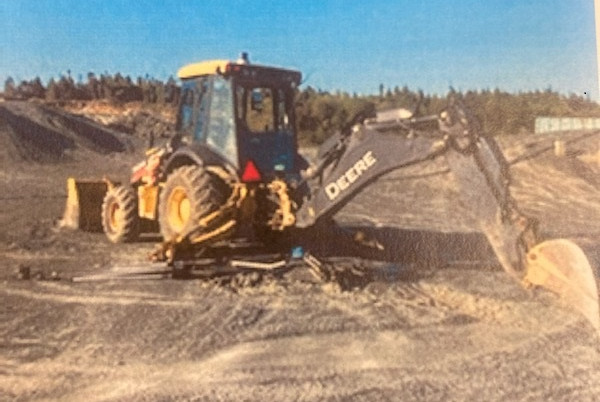 A yellow John Deere backhoe is parked in a sand pit. A blue sky is observed in the background.
