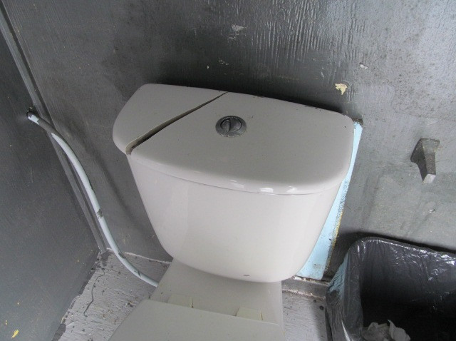 Une toilette blanche avec une fente sur le couvercle du réservoir.