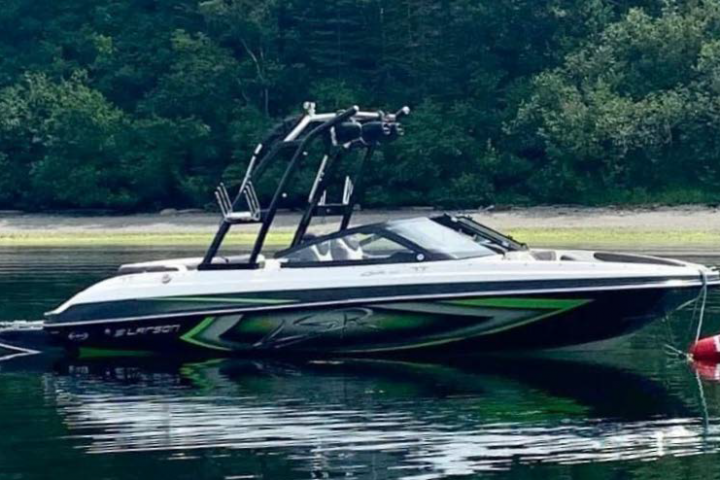 A large black sport boat is seen floating on a pond. The boat is black and neon green. 