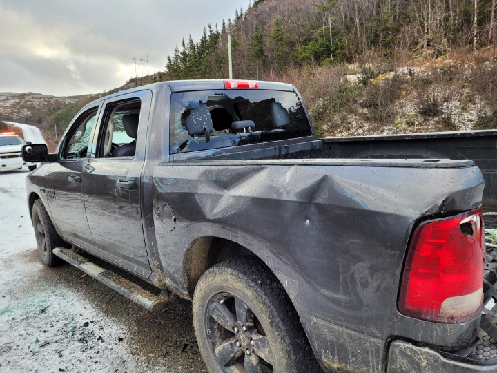 Un camion bleu foncé est montré avec les fenêtres brisées et les panneaux latéraux sévèrement endommagés.