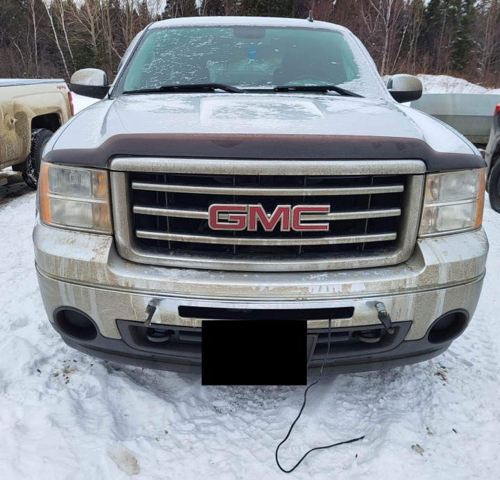 The front grill of a GMC truck is shown, with a wire hanging out from under the front bumper. 