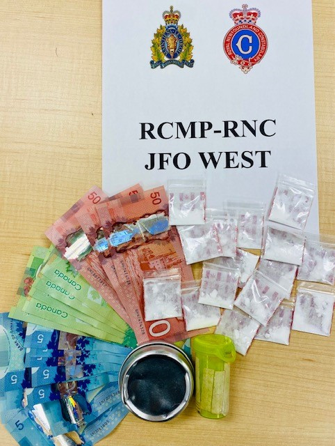 A sign reads 'RCMP-RNC JFO WEST' along with a large quantity of cash, a pill bottle and numerous small baggies of cocaine. 