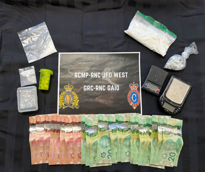 A number of items are displayed on a table, including a quantity of cash, quantities of cocaine and crack cocaine and digital weigh scales, surrounding a sign that says 