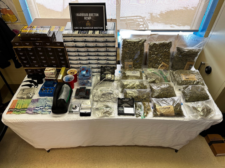 Un certain nombre d'objets, dont de l'argent liquide, du tabac de contrebande, des armes, des balances, des munitions et divers stupéfiants, sont exposés sur une table dans des sacs de preuves.