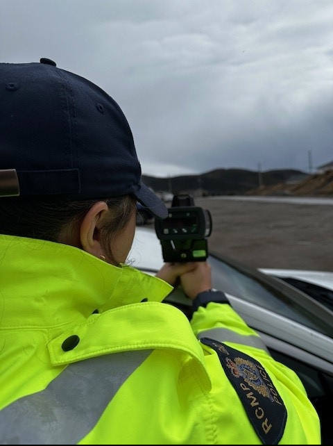 A uniformed RCMP officer is using a hand-held speed detection device.