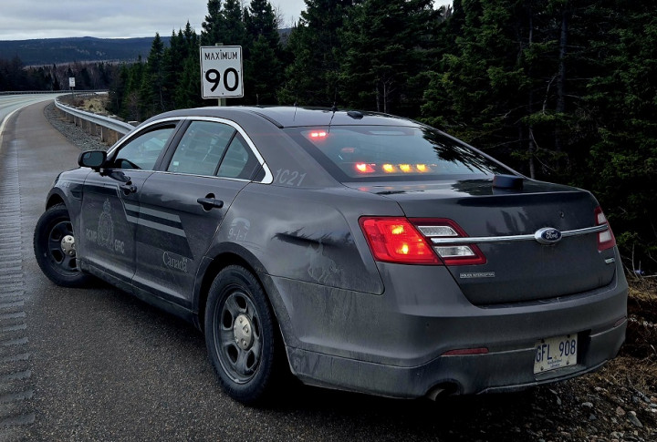 Une voiture de police banalisée garée en bordure de route derrière un panneau où est inscrit la limite de vitesse : 90 km/h.