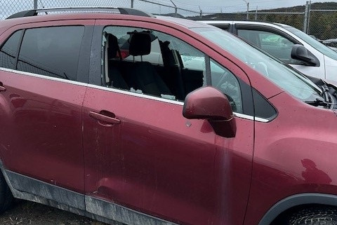 A vehicle is parked in a compound with its front passenger side window smashed out.