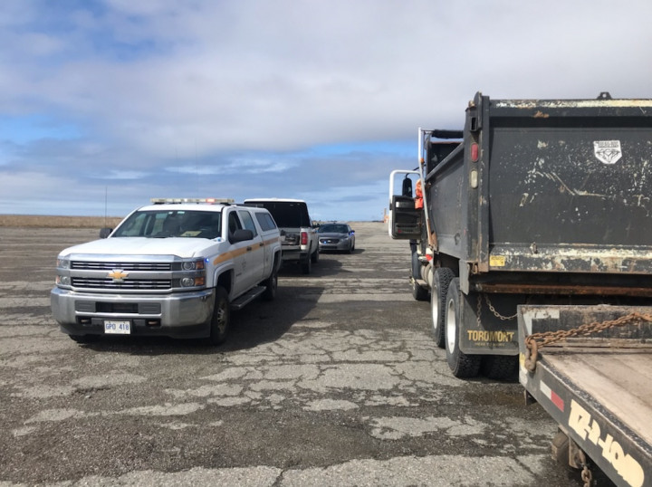 Two Highway Enforcement trucks and an unmarked police vehicle are parked beside a dump truck during the day.