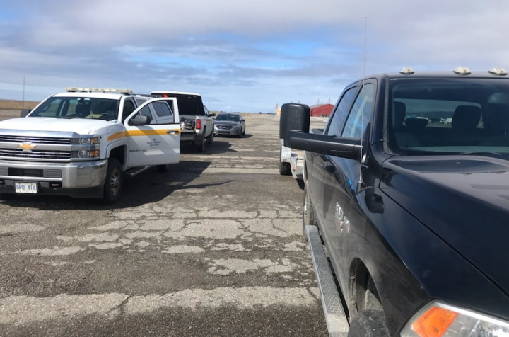 Two Highway Enforcement trucks and an unmarked police vehicle are parked beside a heavy-duty pick-up truck towing a trailer during the day.