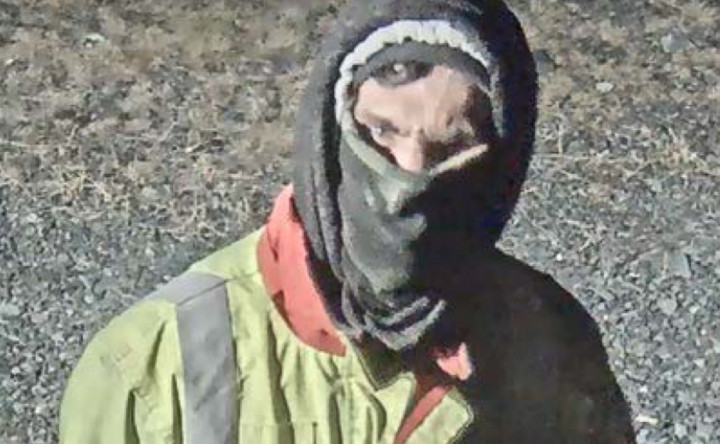 A surveillance image shows an individual from the chest up wearing a high-visibility yellow jacket, a hood over their head and a face covering.
