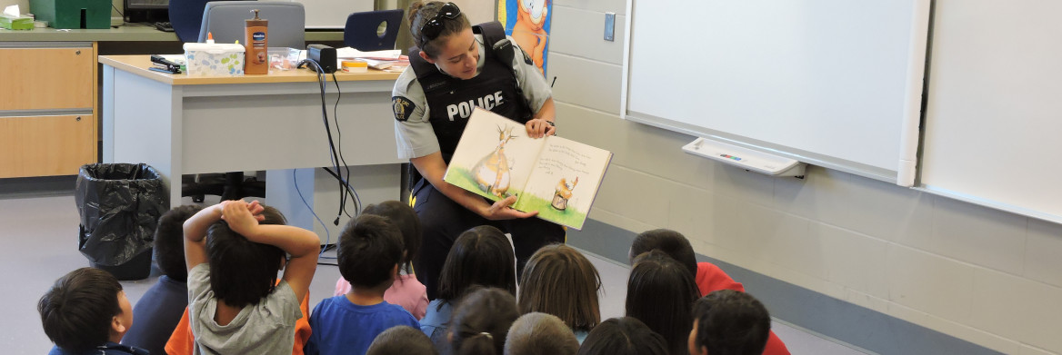 Police officer reading book to students.