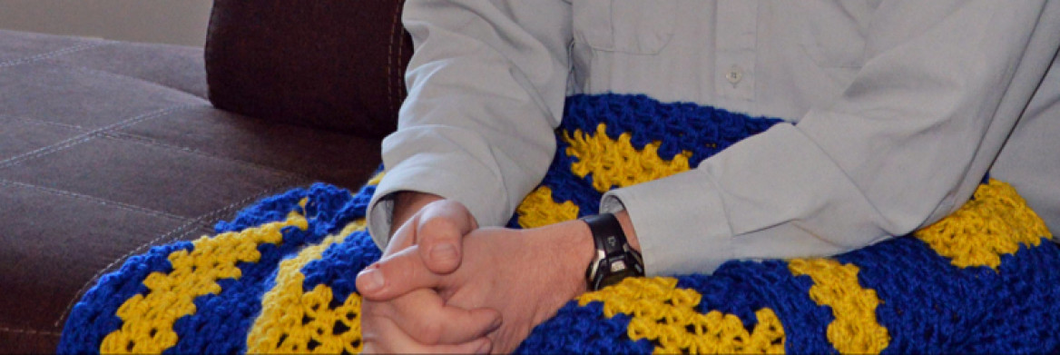 Les mains d'un homme sur une couverture tricotée bleue et jaune.