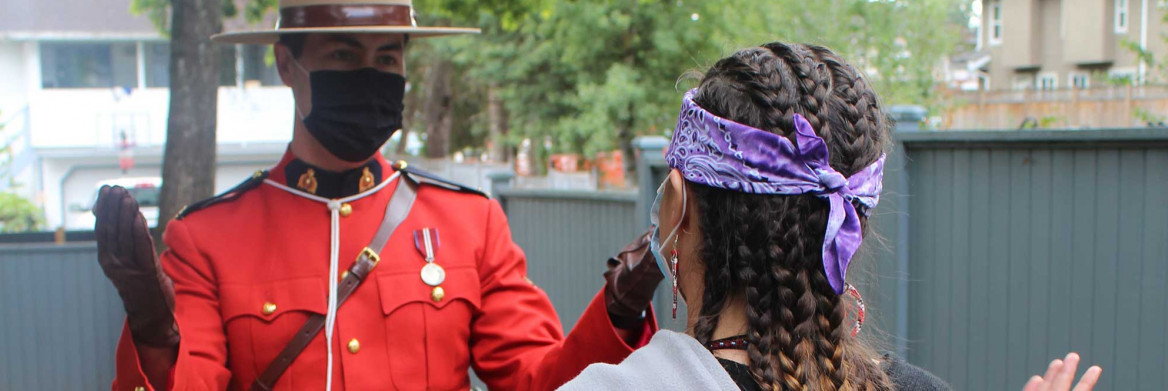 An RCMP officer dressed in Red Serge faces a young person, who is pictured from behind. Both have their hands raised.