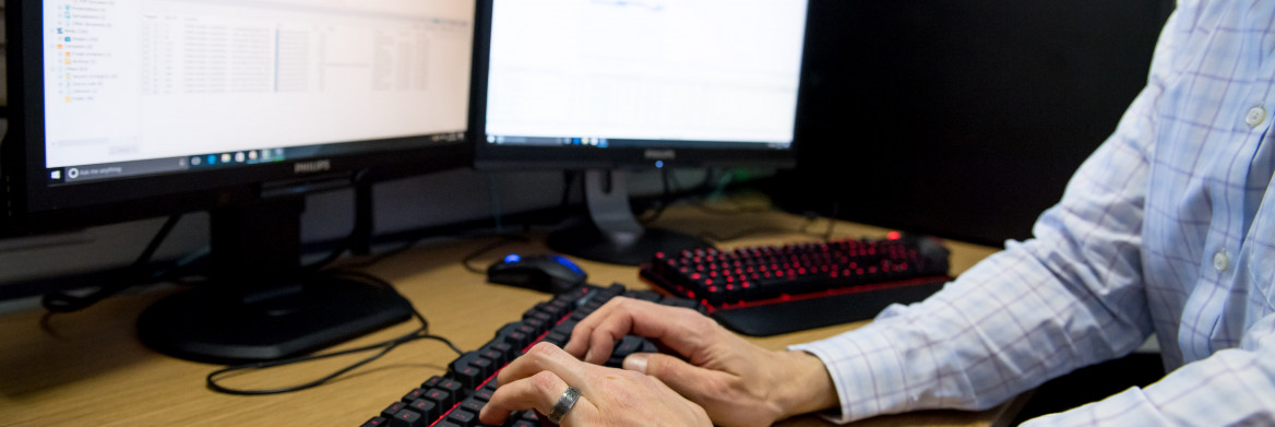 Hands typing on keyboard in front of computer screen.