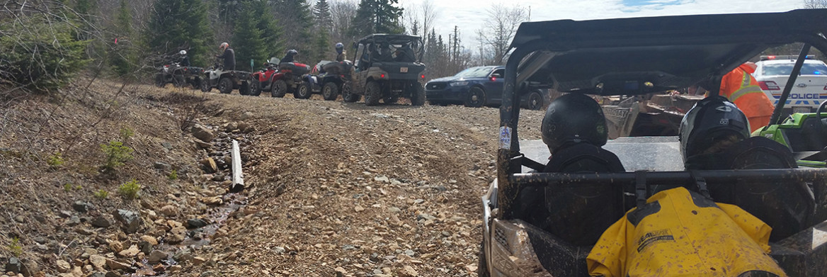 A row of ATVs are on a dirt road. Two RCMP cruisers with their red-and-blue lights on are in the background. 