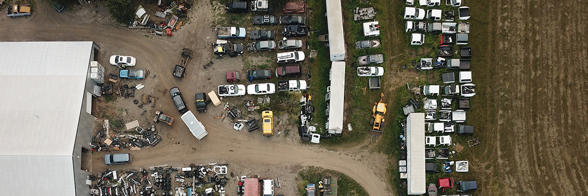 An aerial view of a building with a yard full of car parts and vehicles in states of disrepair. 