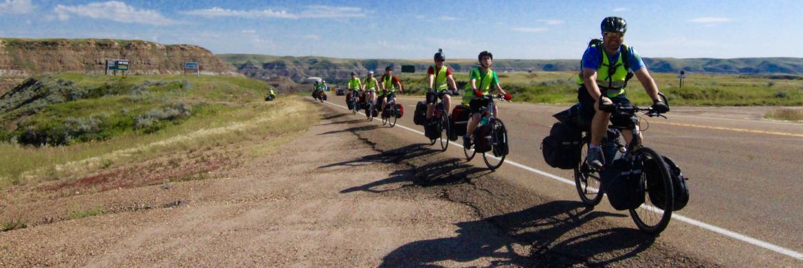 Man and five kids ride bikes on road.