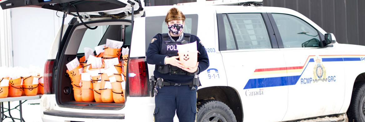 Debout devant un véhicule et masque au visage, une agente de la GRC tient un seau orange qui ressemble à une citrouille d'Halloween. On en voit dizaines d'autres dans le coffre ouvert.