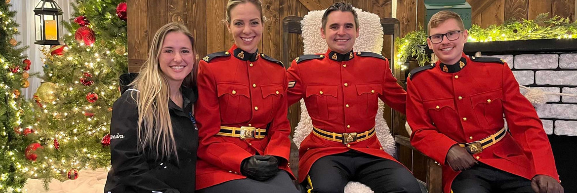 Three RCMP officers in red serge sit next to a young woman.