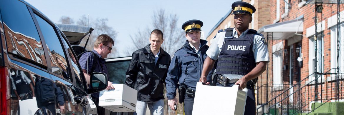 Four police officers carrying computer equipment down a street.