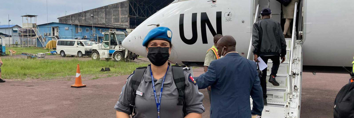 A female RCMP officer wearing a blue beret and a mask stands in front of a UN aircraft.