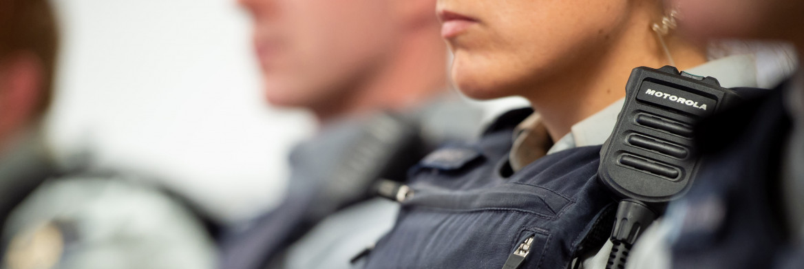 A female RCMP officer wearing her uniform sits in a row of other officers.