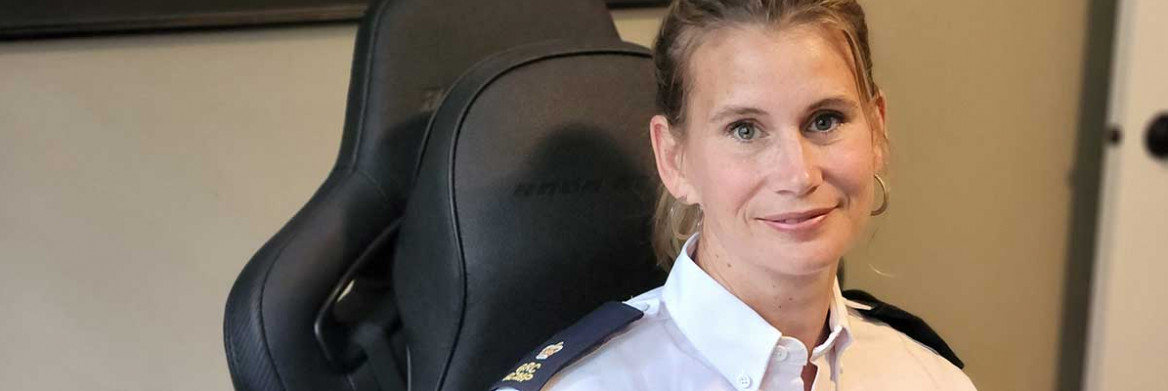 A female RCMP officer sitting at a desk/standing indoors.