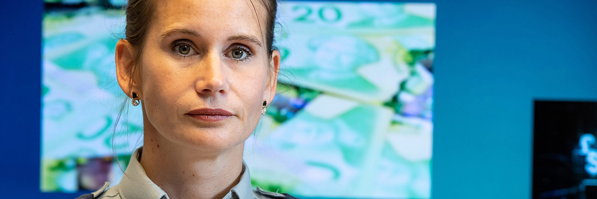 A female RCMP officer stands in front of a large image of Canadian currency.