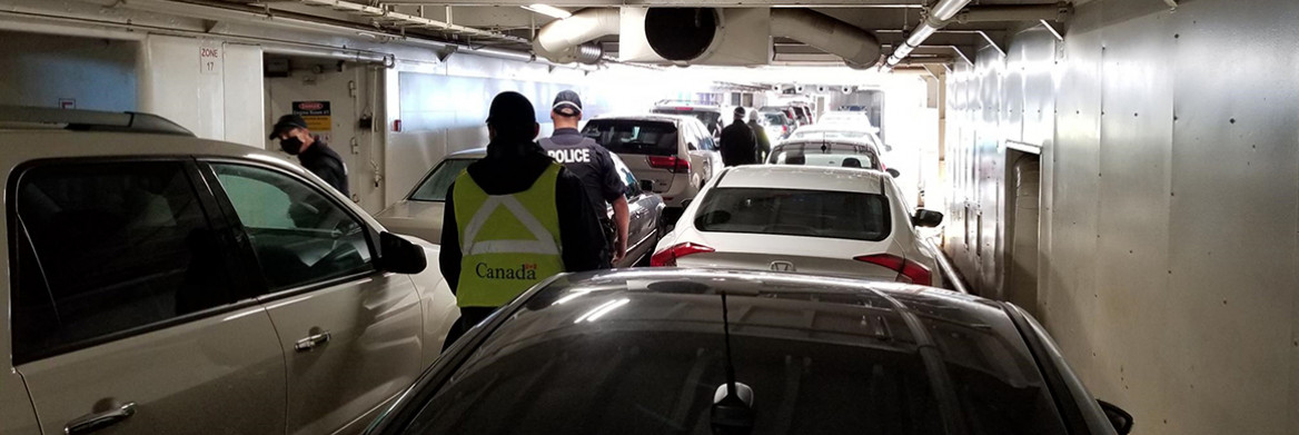Police and other officials walk between cars on an enclosed ferry deck.