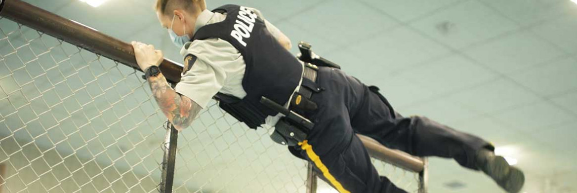 In a gymnasium, an RCMP officer wearing a duty uniform jumps over a fence.