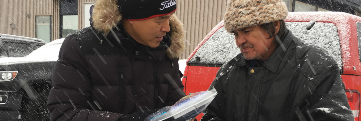 Man offering care package to a homeless man in a snowstorm.