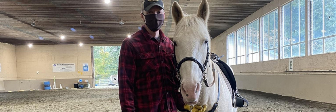 Un homme se tient debout à côté d'un cheval sur un terrain d'entraînement intérieur.
