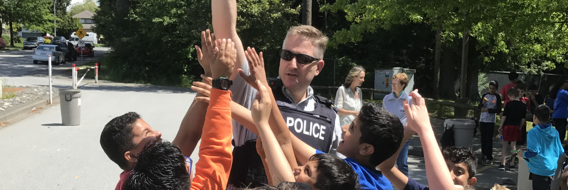 Male police officer surrounded by children reaching their hands up.