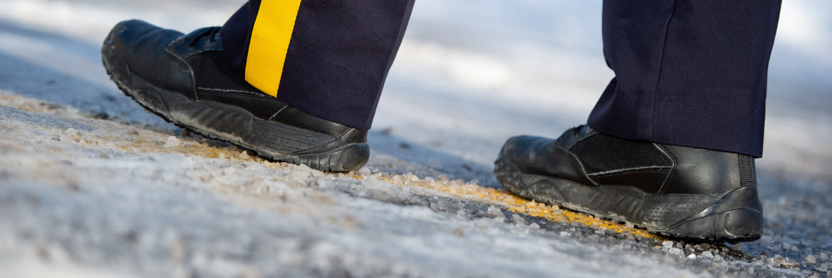 Bottes d'un agent de la GRC qui marche sur une route glacée et enneigée.