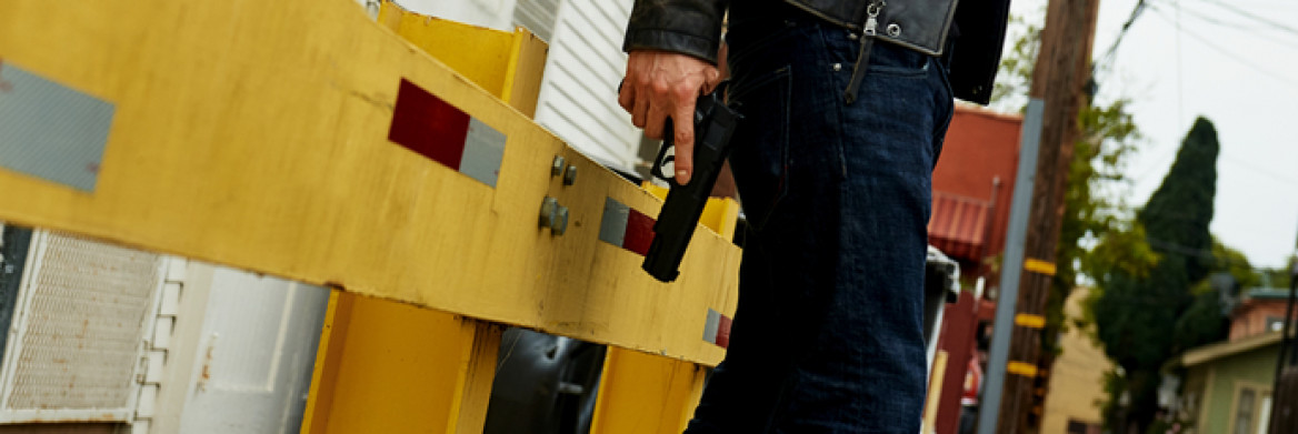 A man holding a handgun in an alley.