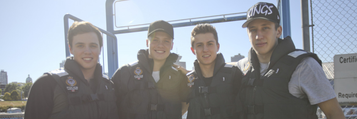 Four young men standing on a boat with city in the background.