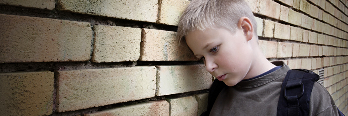 Upset boy leaning against a brick wall. 